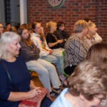 Słuchacze siedzą na krzesłach, skupieni na występie zespołu podczas koncertu w bibliotece.