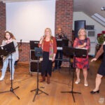 Cztery kobiety z teczkami nutowymi występują na scenie podczas koncertu w bibliotece.