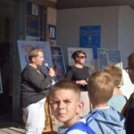 Kobieta z mikrofonem prezentuje plakat podczas spotkania, a przed nią stoi grupa dzieci.