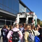 Grupa dzieci zgromadziła się przed śmietnikiem podczas pikniku edukacyjnego promującego alternatywne formy transportu.