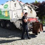 Pracownik komunalny opróżnia pojemnik na śmieci w pobliżu samochodu do odbioru odpadów.
