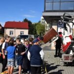 Grupa osób uczestniczy w pikniku edukacyjnym, a obok nich stoi rowerowa czytelnia i sprzęt do demonstracji.