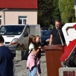 Mężczyzna wyładowuje pojemnik na śmieci przed domem, podczas gdy dziecko stoi obok niego.