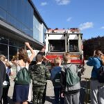 Grupa osób obserwuje policyjny samochód podczas pikniku edukacyjnego.