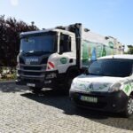 Na parkingu stoi samochód osobowy obok ciężarowego pojazdu do odbioru odpadów.