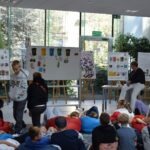 Na prezentacji warsztatowej uczestnicy oglądają tablice z informacjami o roślinach i zwierzętach.