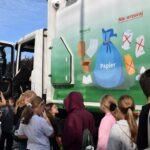 Dzieci obserwują śmieciarkę z grafiką informującą o prawidłowej segregacji odpadów.