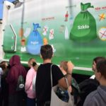 Grupa osób obserwuje mural przedstawiający zasady segregacji odpadów umieszczony na boku śmieciarki.