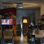 W pomieszczeniu bibliotecznym dzieci siedzą przed telewizorem, na którym wyświetlany jest film edukacyjny.