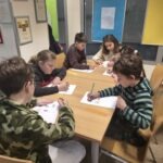 Dzieci siedzą przy stole i piszą, wykonując zadanie związane z zajęciami bibliotecznymi.