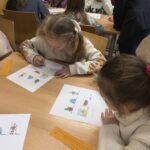 Dzieci pracują nad zadaniem plastycznym na stole w sali bibliotecznej.