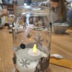 Szkolny lampion z motywem zimowym zawiera świeczkę, która delikatnie oświetla wnętrze słoika.