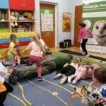 Dzieci bawią się z jeżem leżącym na dywanie podczas zajęć edukacyjnych.