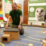 Mężczyzna prezentuje dzieciom drewniany model budki dla jeża podczas warsztatów ekologicznych.