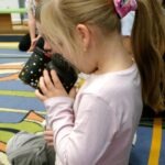 Dziewczynka trzyma aparat fotograficzny, prawdopodobnie robiąc zdjęcia podczas warsztatów.