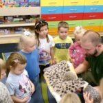 Dzieci z przedszkola obserwują mężczyznę trzymającego jeża owiniętego kocem.