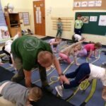 Instruktor pomaga dziecku podczas ćwiczenia z wykorzystaniem sprzętu do rehabilitacji.