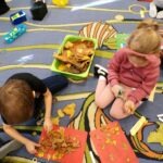 Dzieci układają liście na czerwonym kartonie podczas tworzenia domku dla jeża.