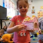 Dziewczynka trzyma w rękach kolorowy domek z liśćmi, który został zbudowany podczas warsztatów dla przedszkolaków.