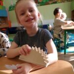 Dziecko prezentuje drewnianego jeżyka wykonanego z drewna i liści podczas warsztatów plastycznych.