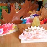 Na drewnianych podstawkach ustawiono kolorowe jeżyki wykonane przez dzieci z liści i drewna.