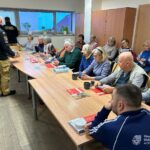 Seniorzy uczestniczą w spotkaniu, podczas którego omawiane są dawne fotografie Chrzanowa oraz przekazywane informacje dotyczące bezpieczeństwa domowego przez Straż Pożarną.