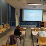 W sali szkoleniowej ustawione są krzesła i stoliki, a na ekranie wyświetlana jest prezentacja.