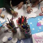 Dzieci tworzą prace plastyczne z wykorzystaniem materiałów do rysowania i wycinania na stole w bibliotece.