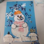 Dziecko stworzyło kolorowy rysunek przedstawiający bałwanka z pomarańczową czapką i szalikiem na tle niebieskiego tła.