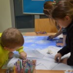 Dzieci wspólnie malują na dużym arkuszu papieru, używając kolorowych kredek.