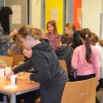 Dzieci siedzą przy stole, układając lampiony podczas zajęć w bibliotece.