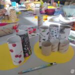 Na żółtej powierzchni leżą kartonowe tubki ozdobione motywami świątecznymi i innymi wzorami.