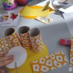 Dzieci tworzą ozdobne tubki z papieru podczas warsztatów plastycznych w bibliotece.