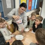 Nauczycielka podczas eksperymentu wlewa proszek do miski z wodą, obserwując reakcję dzieci.