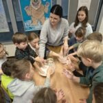 Dzieci z zainteresowaniem obserwują dorosłą osobę podczas eksperymentu związanego z cieczą nienewtonowską.