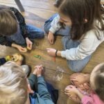 Dzieci siedzą na drewnianej podłodze, bawiąc się drobnymi przedmiotami imitującymi przyprawy.