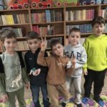 Pięciu chłopców stoi przed regałami z książkami, prezentując uśmiechy i gesty dłonią.