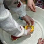 Dziecięce ręce trzymają żółty i szary element konstrukcyjny w białej misce z wodą.