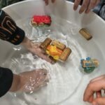 Dziecięce ręce zanurzone są w białej cieczy, trzymając model statku zbudowanego z kanapek.