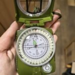 W dłoni widoczny jest kompas z zielonym korpusem i przezroczystą osłoną.