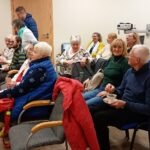 Uczestnicy spotkania Dyskusyjnego Klubu Filmowego siedzą na krzesłach i słuchają prezentacji.