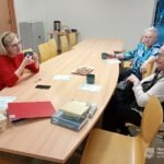 Uczestnicy spotkania siedzą przy długim stole konferencyjnym, otoczeni książkami i kubkami z napojami.