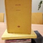 Żółty tomik poezji Rilke spoczywa na stosie książek.