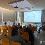 Uczestnicy warsztatów siedzą w sali, skierowani na wyświetlacz z prezentacją.