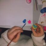 Dziecięce ręce malują farbami gwiazdki na białym papierze podczas warsztatów plastycznych.