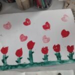 Dziecięca praca przedstawia czerwone tulipany na zielonym tle z różowymi sercami rozrzuconymi powyżej.