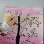 Dziecko rysuje czarny markerem gałęzie na papierze z różowym tłem.