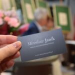 W dłoni widoczna jest wizytówka Mirosława Janika z danymi kontaktowymi i adresem strony internetowej.