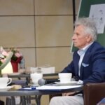 Mirosław Janik siedzi przy stole w trakcie Akademii Słowa, otoczony filiżankami i mikrofonem.