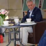 Mężczyzna w marynarce siedzi przy stole z filiżankami, podczas spotkania Akademii Słowa.